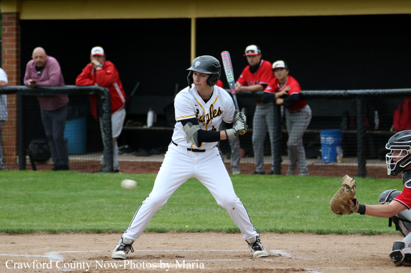 Baseball batter in white uniform and black helmet at home plate, swinging at a pitched ball with catcher in red gear crouched behind.