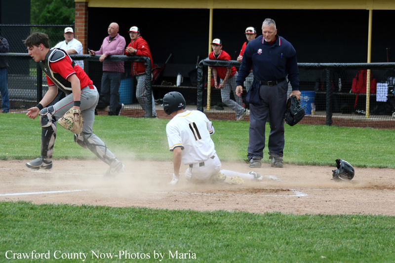 Baseball: runner slides into home plate as catcher and umpire watch, dust rises on the infield dirt.