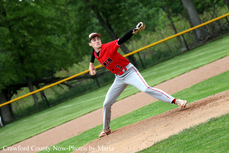 Baseball pitcher in a red uniform winds up on the mound to throw a pitch during a game.