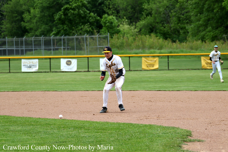 Baseball infielder in a white uniform fields a ground ball on the infield dirt with a teammate in the background.