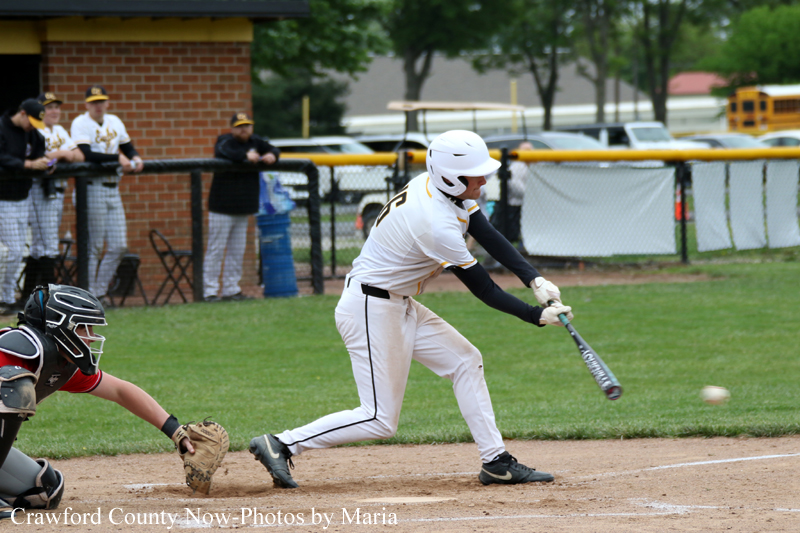 Baseball batter in white uniform swings at an incoming pitch near home plate, with the catcher crouched behind him.