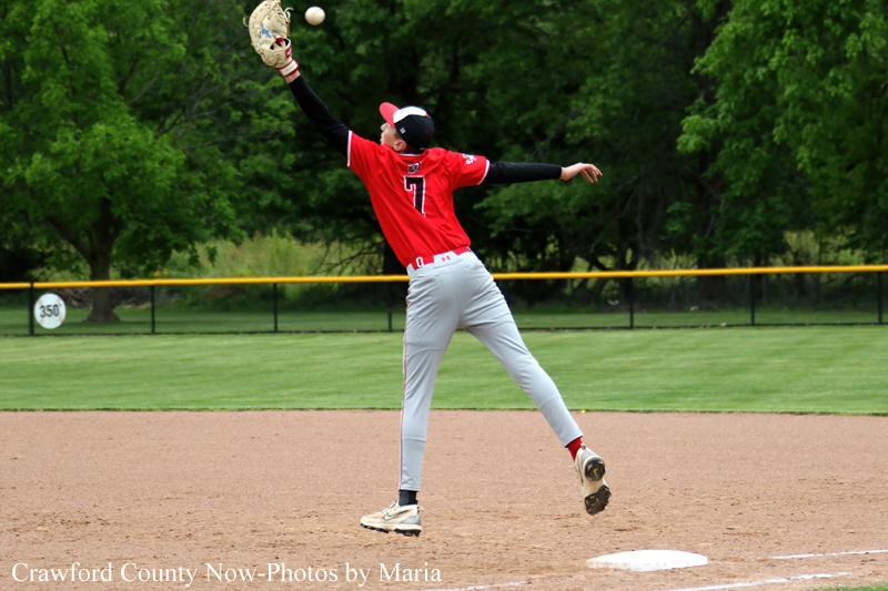 Baseball pitcher in a red uniform throws a pitch on the infield with glove raised and ball in the air.