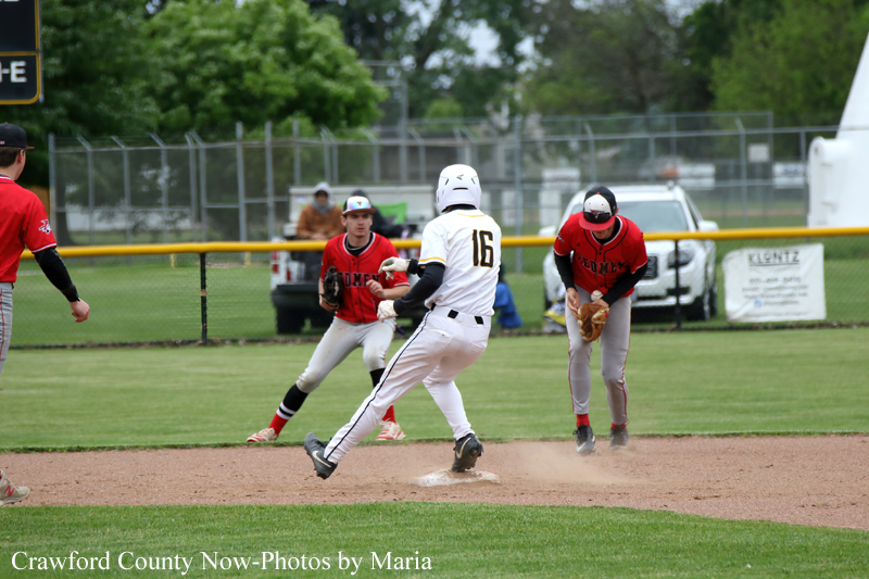 Baseball play: white-uniform runner (#16) slides toward second base as a red-uniform fielder approaches the bag; another red fielder watches nearby on the infield dirt.