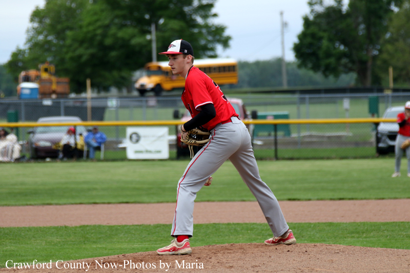 Baseball pitcher in a red uniform winds up on the mound during a game, glove ready to throw.