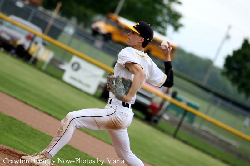 Baseball pitcher in white uniform delivering a pitch on a field with a dirt mound and green outfield in background, glove ready