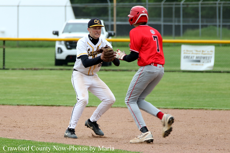 Baseball infielder in white uniform with a black cap tags a baserunner in red near a base on the dirt infield.