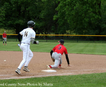 Baseball scene: a runner in red slides into second base as the white-uniformed fielder approaches; ball near the infield dirt.