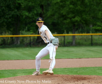 Baseball pitcher in a white uniform with CC on the cap, mid-pitch on the mound with green outfield behind him.