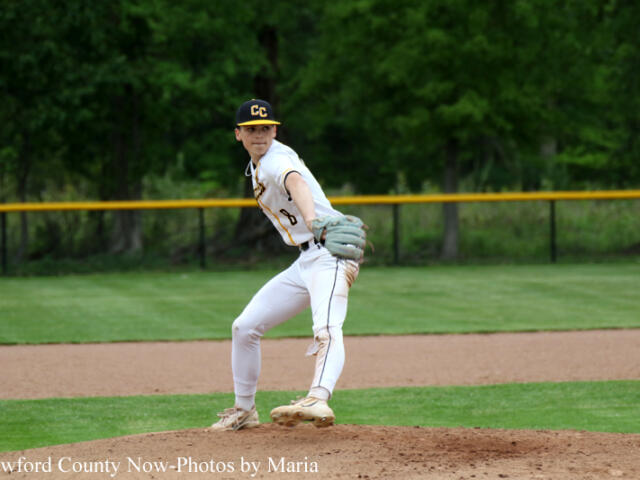 Baseball pitcher in a white uniform with CC on the cap, mid-pitch on the mound with green outfield behind him.
