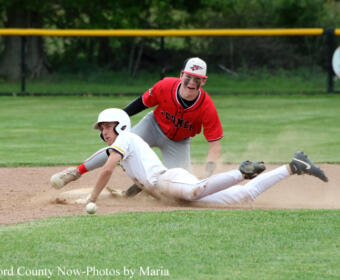 Two baseball players collide at a base: a white-uniform runner slides headfirst while a red-uniform fielder reaches to tag him.