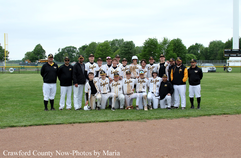 Group of baseball players in white and black uniforms posing for a team photo on the field with coaches nearby.