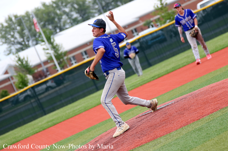 Baseball pitcher in a blue uniform delivering a pitch on the mound as a fielder watches in the infield.