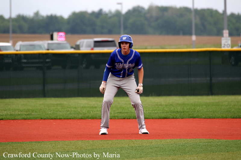 Baseball player in a blue uniform and helmet stands in a ready fielding position on the infield dirt.