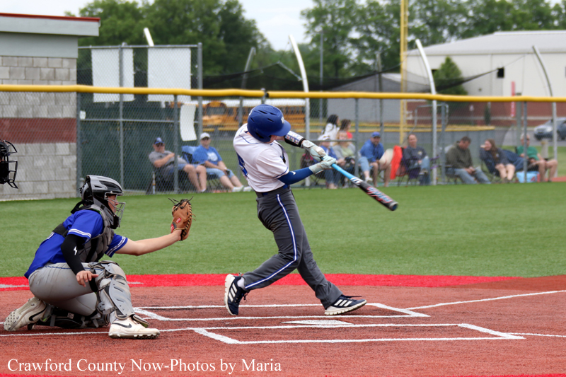 Baseball batter swinging at a pitch as the catcher crouches behind home plate; audience sits beyond the fence.