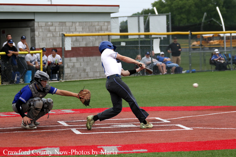 Baseball batter in white swings at a pitch at home plate while the blue-clad catcher crouches behind him.