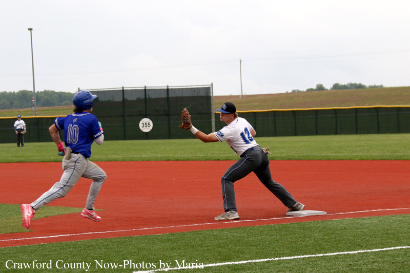 Baseball players: a fielder in white reaches to tag a baserunner in blue (#10) as he runs toward a base on the red dirt infield.