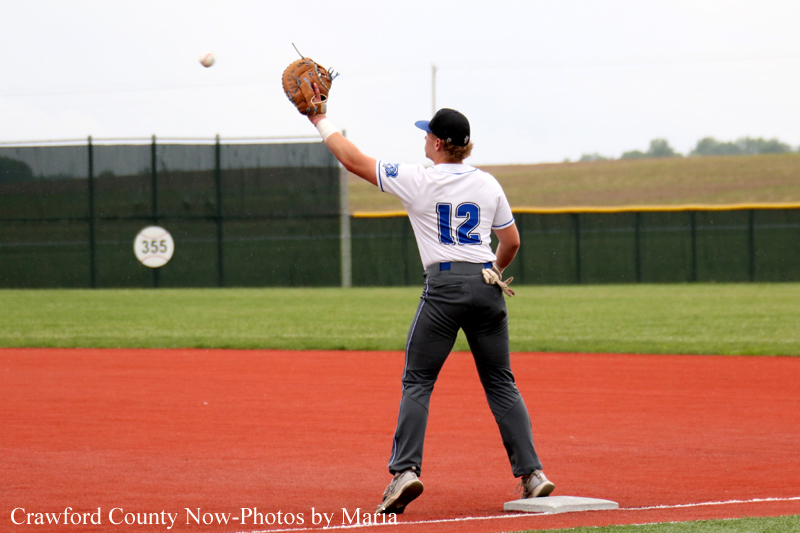Right-handed baseball player wearing number 12 on a red dirt infield, throwing a ball during a game.