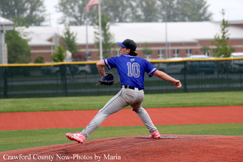 Baseball pitcher in a blue jersey #10 winds up to throw from the mound on a sunny field.
