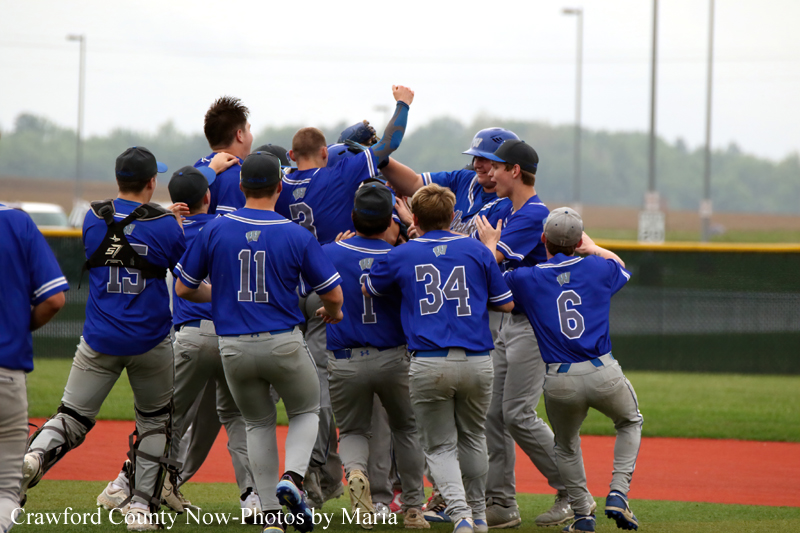 Youth baseball team in blue uniforms celebrating together on the field.