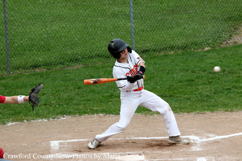 Young baseball player in a white uniform and black helmet swings at a pitch at home plate in a game state.