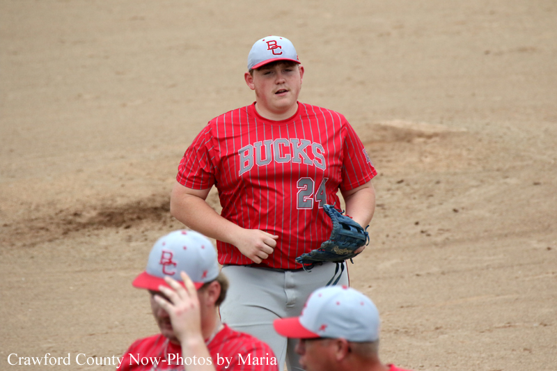 Teenage baseball player in a red Bucks jersey (#24) running on the dirt field with a glove in hand during a game