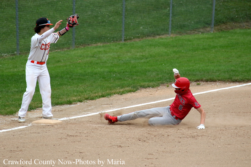 Baseball baserunner in red slides into a base while a fielder in white watches from the bag.