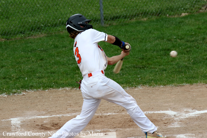 Baseball batter in a white uniform and black helmet swings at a pitched ball on a dirt field, ball approaching the bat.