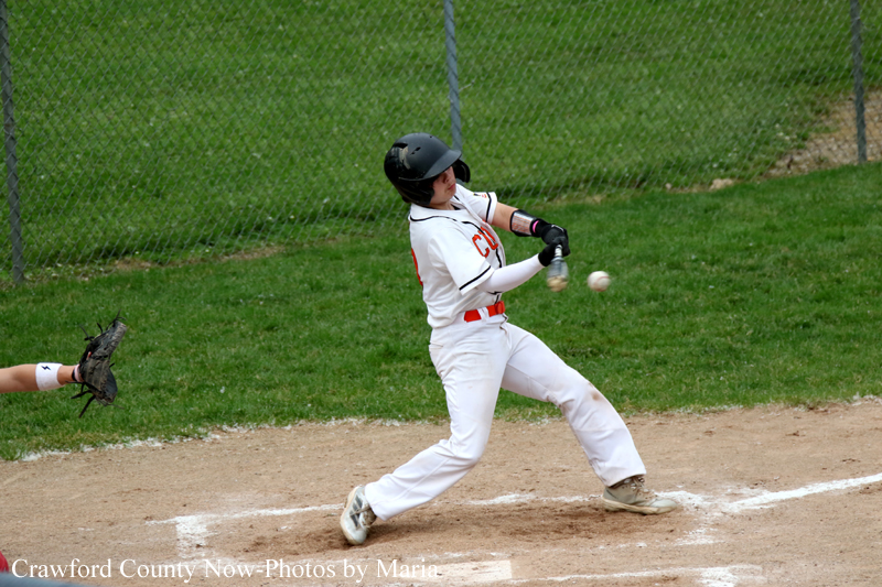 Baseball batter in a white uniform swings at a pitched ball on a dirt field, helmeted and focused on contact.