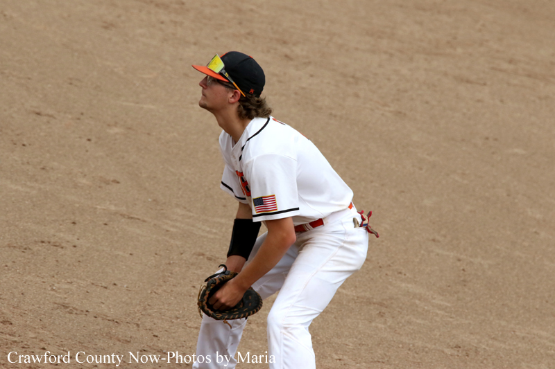 Baseball infielder in a white uniform crouches with glove ready on the dirt infield.