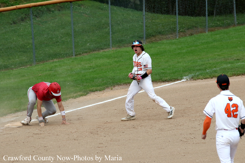 Baseball scene: a baserunner in red slides into a base while a teammate in white shouts in excitement on the dirt infield.