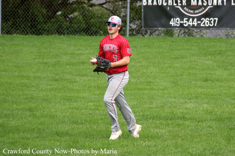 Baseball player in a red uniform with glove on a grassy baseball field, ready to catch a ball.