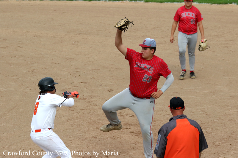 Baseball pitcher in red uniform mid-pitch facing the batter on a dirt infield.
