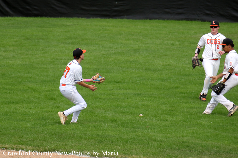 Baseball players in Cubs uniforms on a grassy field; a fielder extends to catch a ground ball while two teammates watch nearby.
