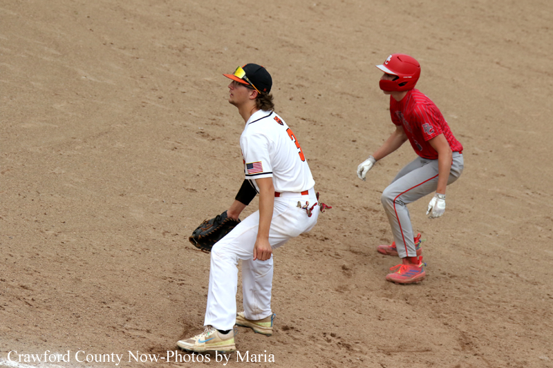 Baseball scene: a white-uniform infielder crouches on dirt as a red-uniform baserunner approaches.