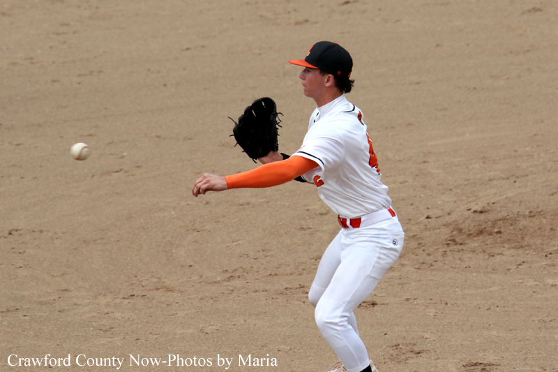 Baseball pitcher in a white uniform with orange sleeves winds up to throw on a dirt mound.