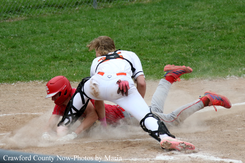 Baseball action: a catcher in white gear slides while a runner in red starts to collide at a dusty base, kicking up dirt on the infield.