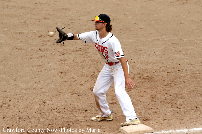 Baseball infielder in a white Cubs uniform fields a ground ball with his glove extended on a dusty infield near first base.