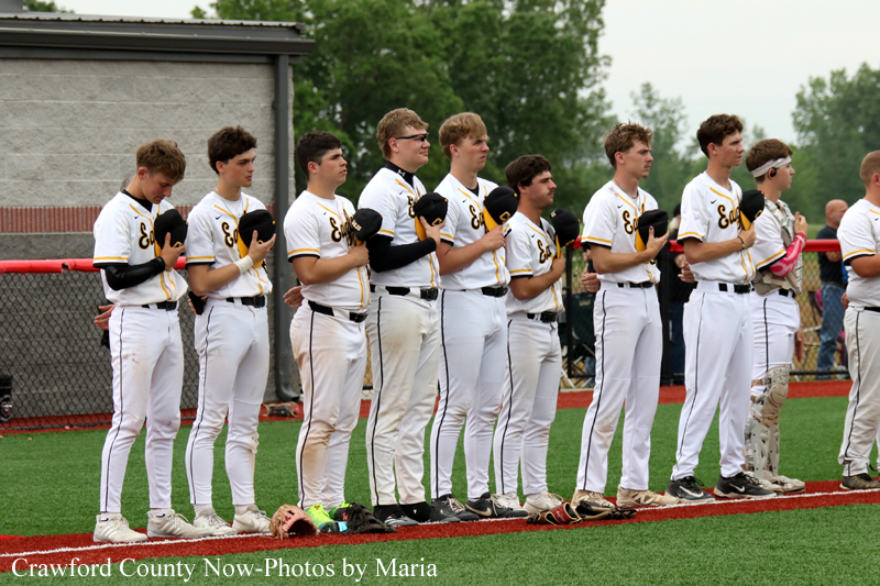 Baseball team in white uniforms standing in a line on the field with hands over their hearts during the national anthem.
