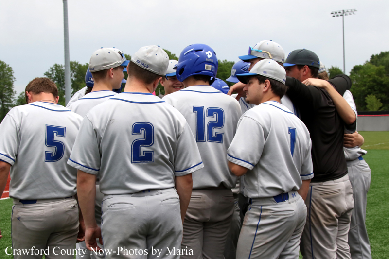 Baseball players in gray uniforms form a huddle on a field, backs visible with numbers 5, 2, 12, and 1.