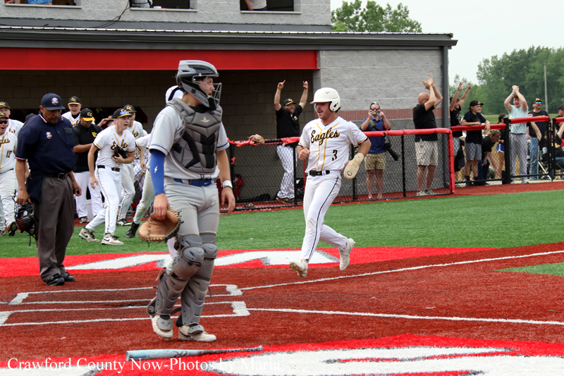 Baseball catcher in gray protective gear at home plate as a runner in a white Eagles uniform slides in, fans cheering behind the fence.
