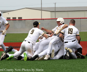Baseball players in white uniforms celebrating in a pile on the field after a play