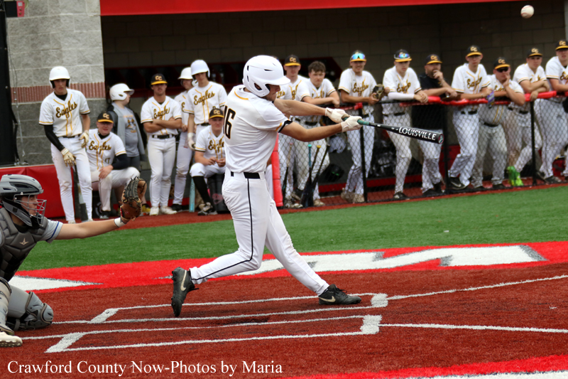 Baseball batter in a white uniform swings at a pitch near home plate as the catcher watches from the left with teammates in the dugout behind the fence.