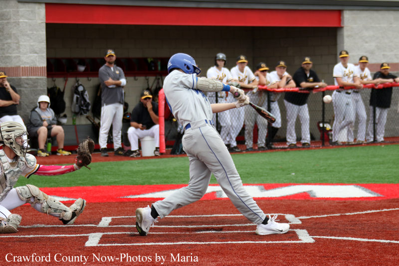 Baseball scene: batter in gray uniform swings at a pitch as catcher in gear reaches to tag the ball, with teammates watching from the dugout.