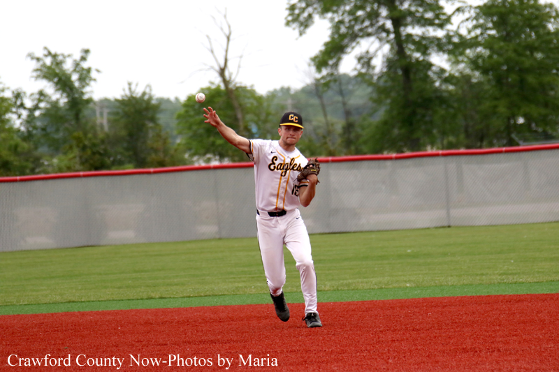 Baseball pitcher in a white Eagles uniform throws a pitch on a red dirt infield with a green outfield and fence behind him.