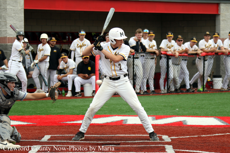 Baseball batter in white uniform at home plate about to swing, with catcher in gray gear crouched behind. Team dugout in background.
