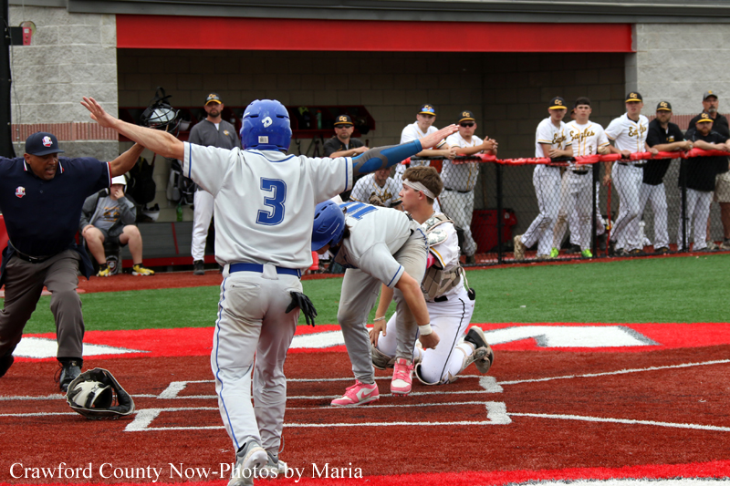 Baseball play at home plate: baserunner in gray with number 3 extends his arm as the catcher in white kneels; umpire and teammates watch from the dugout.