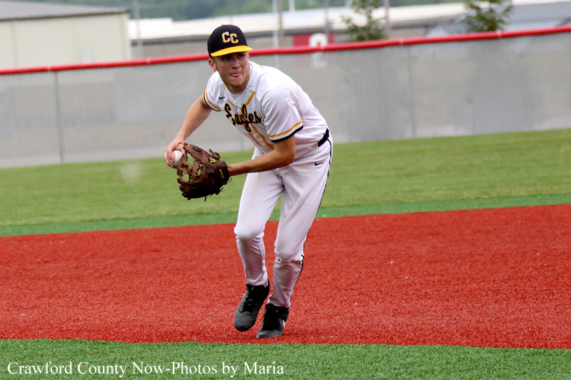 Baseball pitcher in white uniform fields a ground ball on a red infield.