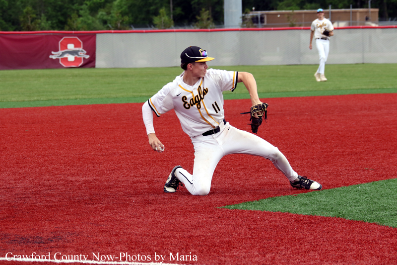 Baseball player in a white Eagle uniform slides on red infield during a game, glove ready at his side.