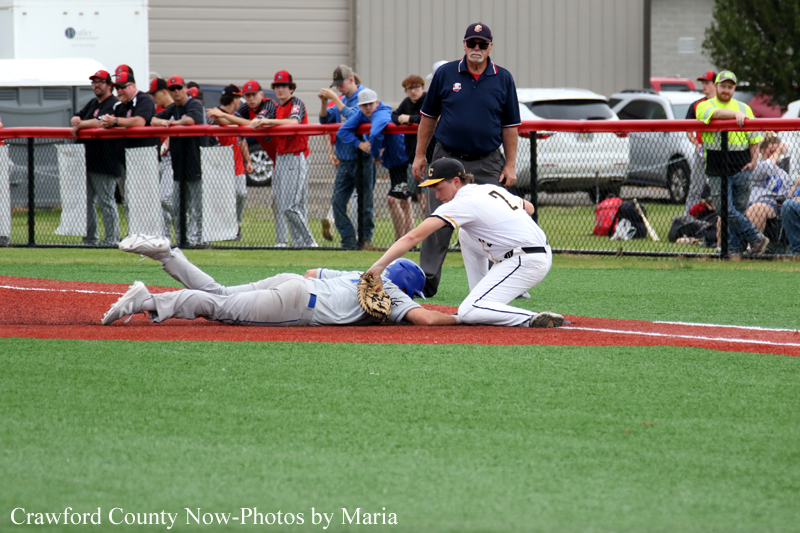 Baseball action: fielder in white tags a sliding baserunner at the base while an umpire watches; crowd behind the fence.