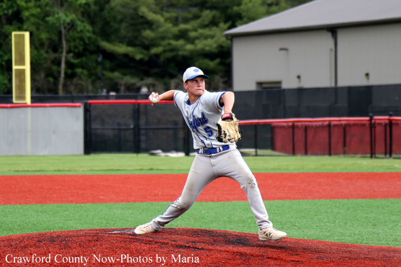 Baseball pitcher in a gray and blue uniform mid-throw from the mound on a red infield.